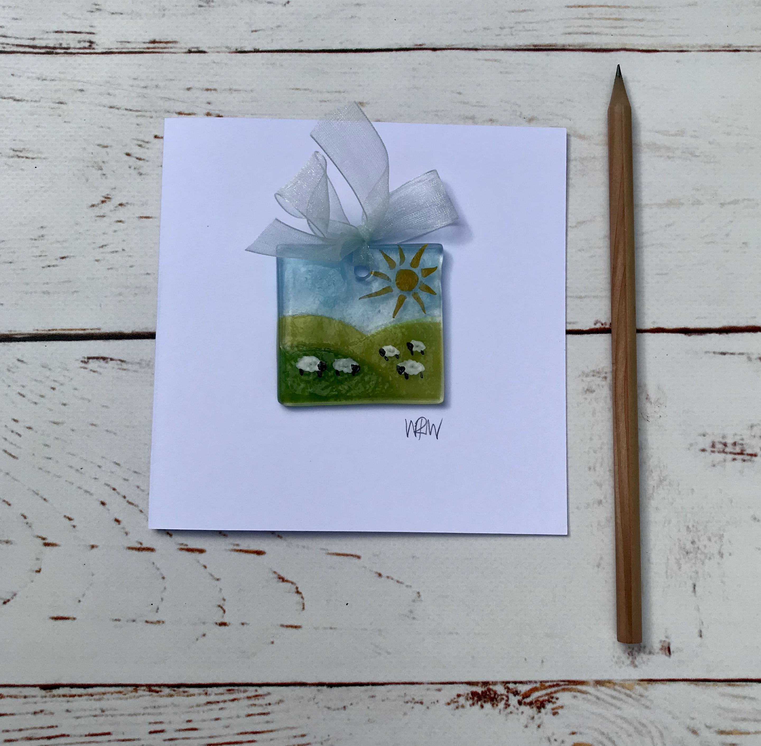 Blank greetings card with tiny glass sheep on hills suncatcher