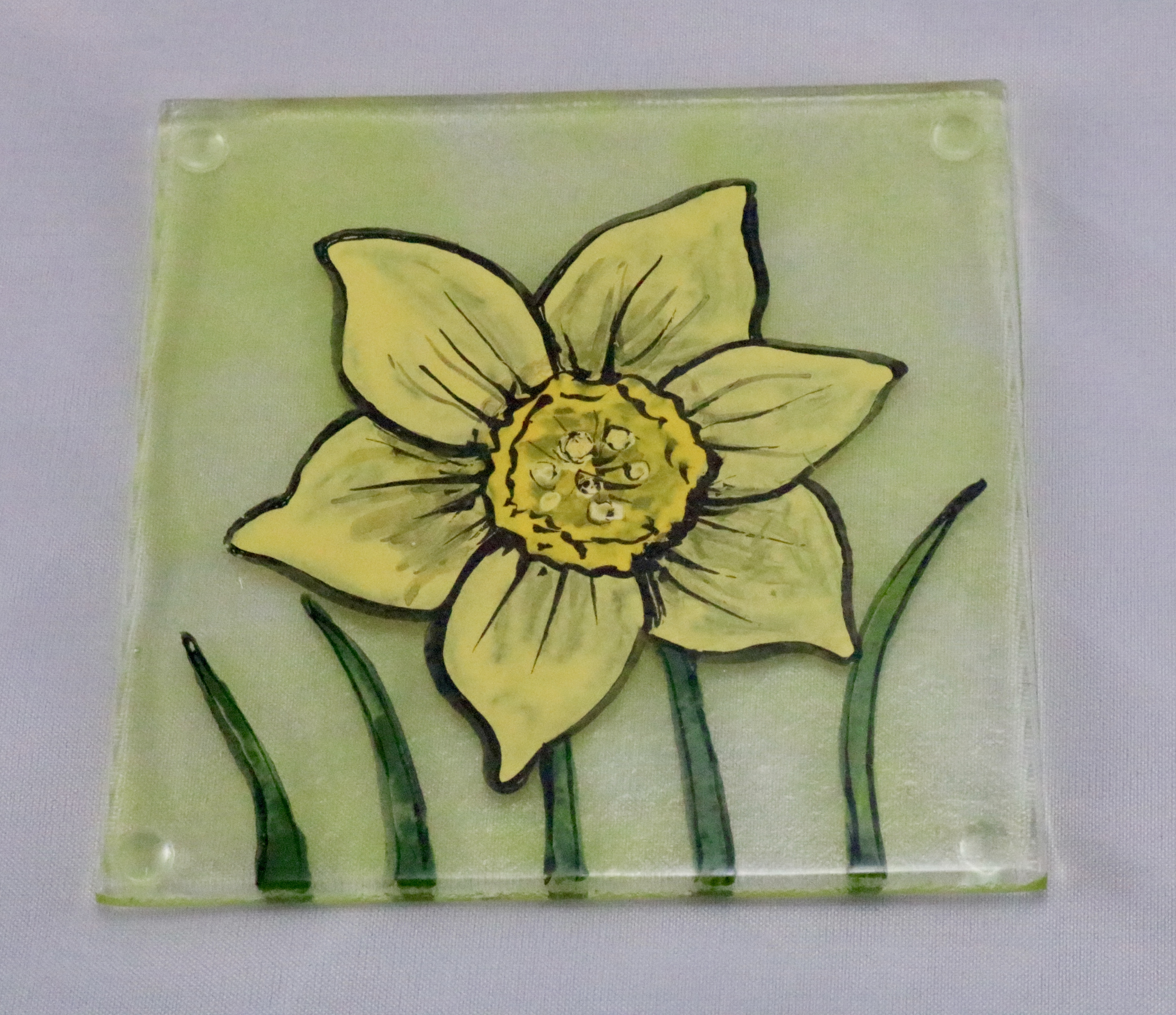 Fused glass coaster of hand painted daffodil on transparent spring green background