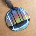 Round fused glass suncatcher with handpainted trees on colourful sunrise background