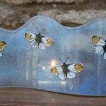 Orange tipped butterflies on a fused glass panel, illuminated by a tealight candle
