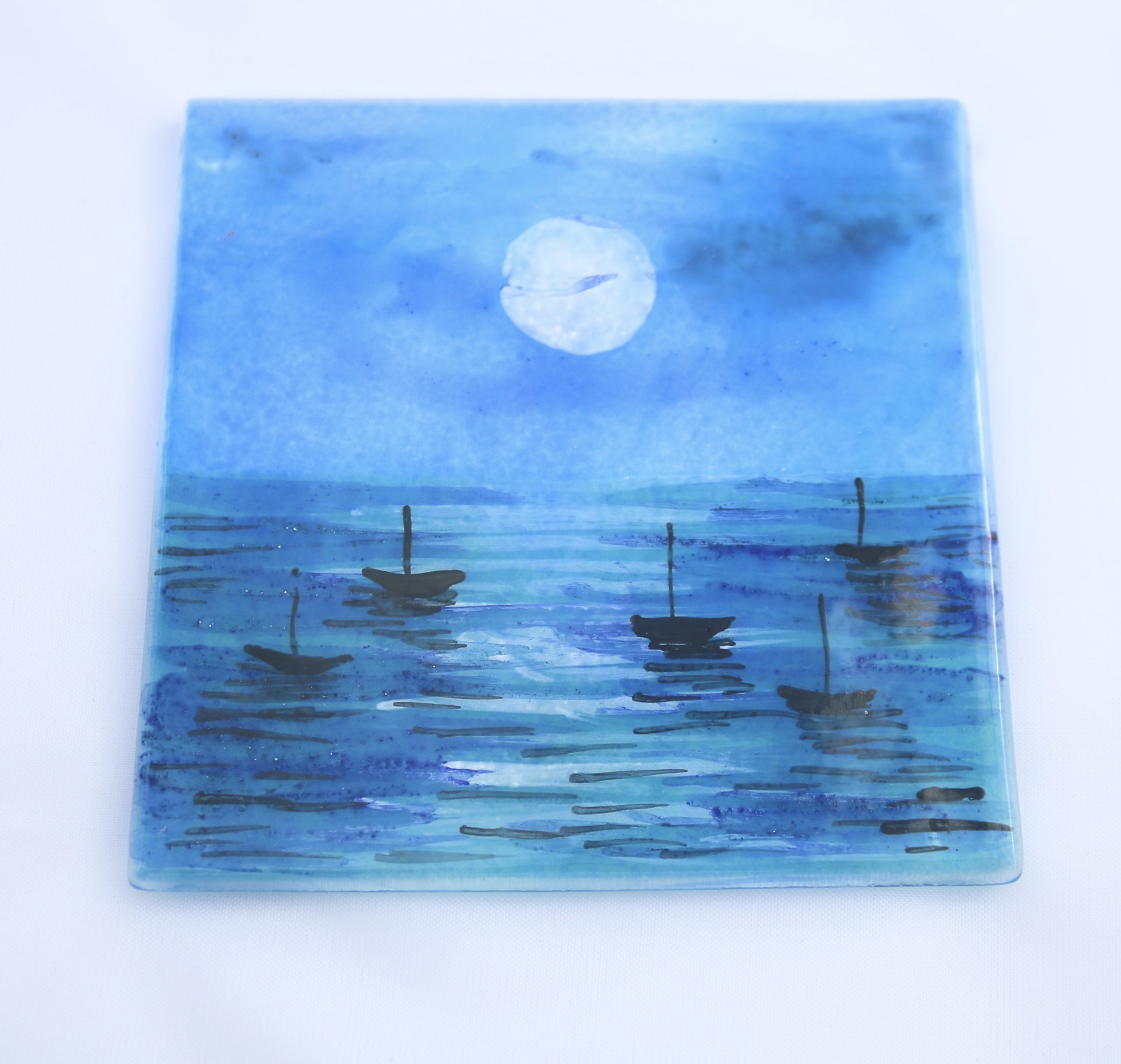 Fused glass coaster with moon lit sea and silhouettes of boats.